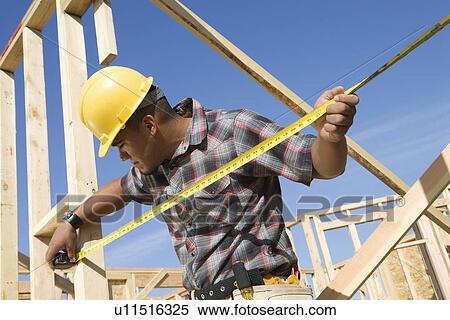 Stock Photography - Construction worker measuring half constructed wall with tape measure. Fotosearch