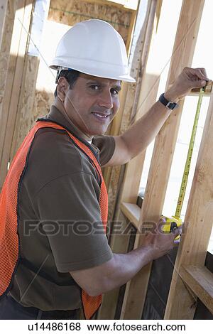 Construction worker measuring wall with measure taper inside half constructed house View Large Photo Image Stock Photo - Construction worker measuring wall with measure taper inside half constructed house. Fotosearch