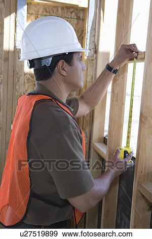 Stock Photo - Construction worker measuring wall with measure taper inside half constructed house. Fotosearch