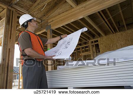 Stock Photo - Construction worker observing half constructed house while holding blueprints. Fotosearch