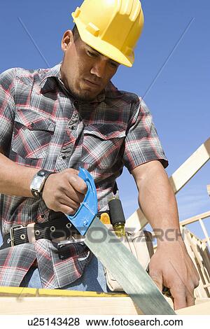 Stock Photo - Construction worker sawing on construction site. Fotosearch