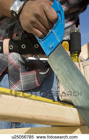 Stock Photography - Construction worker sawing on construction site. Fotosearch