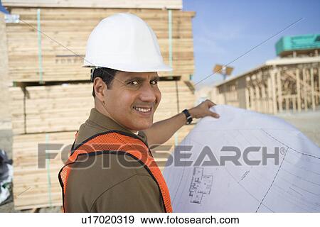 Stock Photo - Construction worker standing on construction site and holding blueprints. Fotosearch