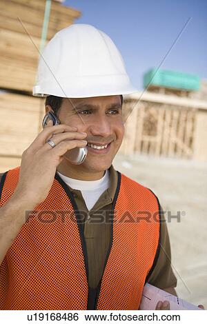 Construction worker standing on construction site and talking in mobile phone View Large Photo Image Stock Photograph - Construction worker standing on construction site and talking in mobile phone. Fotosearch