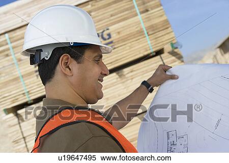Stock Photography - Construction worker standing on construction site and holding blueprints. Fotosearch