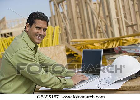 Stock Photo - Construction worker using laptop, portrait. Fotosearch