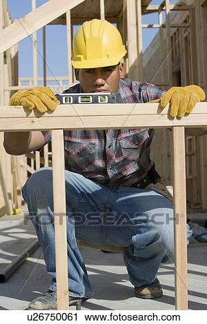 Stock Image - Construction worker using spirit level on building. Fotosearch