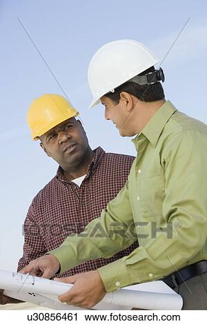Stock Image - Construction workers studying blueprints outdoors. Fotosearch
