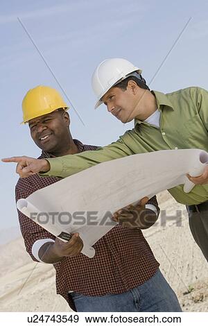 Stock Photo - Construction workers studying blueprints outdoors. Fotosearch