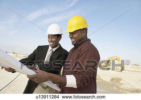 Construction Workers wearing hard hats, looking at plan on Site View Large Photo Image Picture - Construction Workers wearing hard hats, looking at plan on Site. Fotosearch