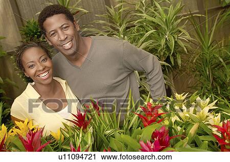 Stock Image - Couple among plants at nursery, (portrait). Fotosearch