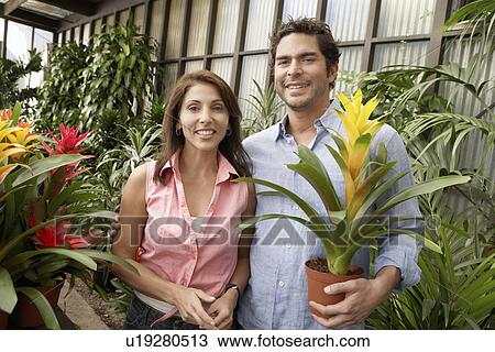 Stock Image - Couple at plant nursery, smiling, (portrait). Fotosearch
