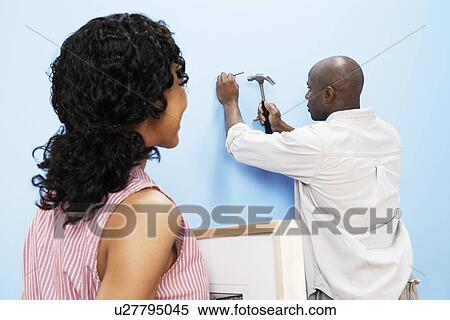 Stock Photography - Couple hanging picture on interior wall, back view. Fotosearch