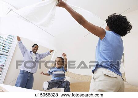 Stock Photo - Couple holding bed sheet over son (3-6). Fotosearch