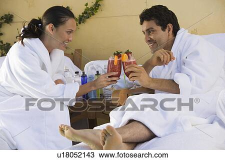 Stock Image - Couple in bathrobe, drinking cocktails outdoors. Fotosearch