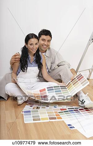 Stock Photo - Couple looking at paint colour samples, sitting on floor, portrait. Fotosearch