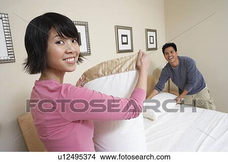 Picture - Couple making bed together, portrait. Fotosearch