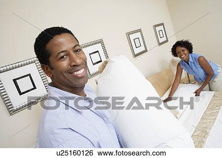 Stock Photograph - Couple making bed together, portrait. Fotosearch