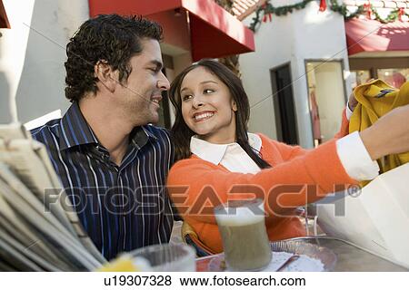 Couple sitting in cafe, woman showing clothing purchase to partner View Large Photo Image Stock Photo - Couple sitting in cafe, woman showing clothing purchase to partner. Fotosearch