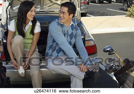 Stock Photograph - Couple Sitting on Rear Bumper of Car Putting on Golf Shoes. Fotosearch