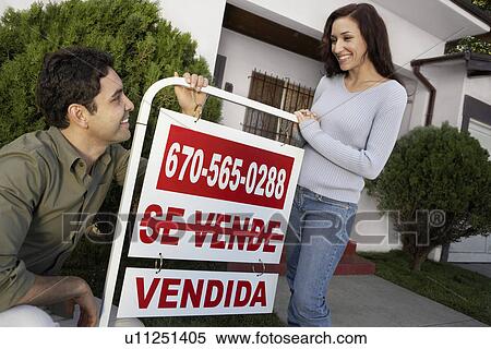 Stock Photography - Couple standing in front of house with Sold sign, portrait. Fotosearch
