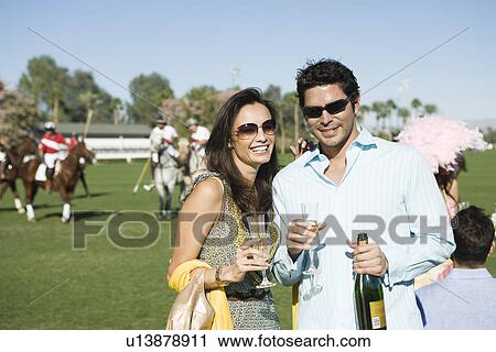 Stock Image - Couple toasting on polo field, portrait. Fotosearch