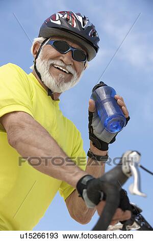 Stock Image - Cyclist drinking from bottle of water, portrait, low angle view. Fotosearch