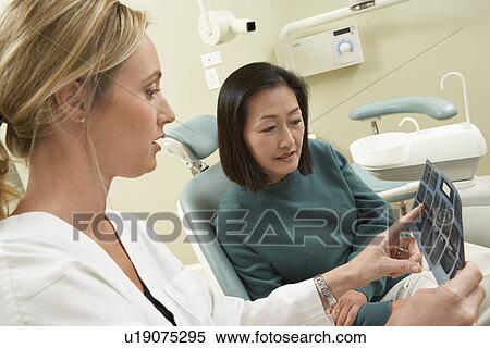 Stock Photography - Dentist and patient examining X-ray in surgery. Fotosearch