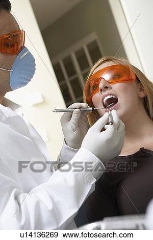Stock Photo - Dentist examining womans teeth in surgery. Fotosearch