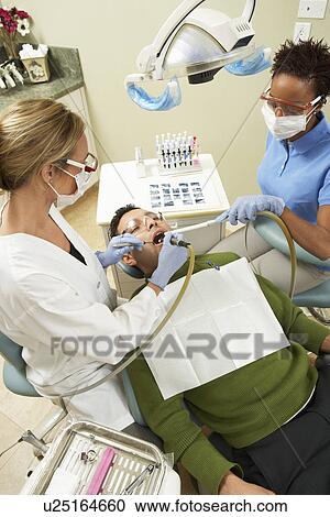 Stock Image - Dentists examining male patient in surgery. Fotosearch