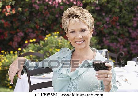 Elegant mature woman sitting in garden, holding wine glass, View Large Photo Image Stock Image - Elegant mature woman sitting in garden, holding wine glass,. Fotosearch