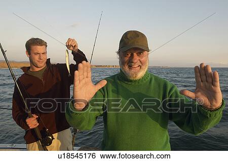 Stock Photograph - Father gesturing fish size on boat, (portrait). Fotosearch