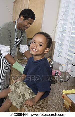 Father washing dishes, son sitting on kitchen counter and smiling View Large Photo Image Stock Photograph - Father washing dishes, son sitting on kitchen counter and smiling. Fotosearch
