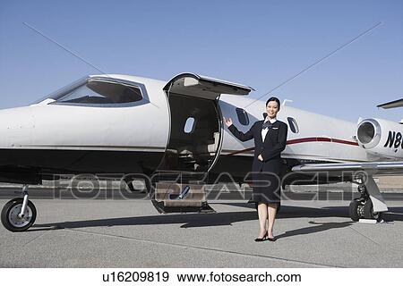 Stock Photo - Female flight attendant standing in front of private jet on runway.. Fotosearch