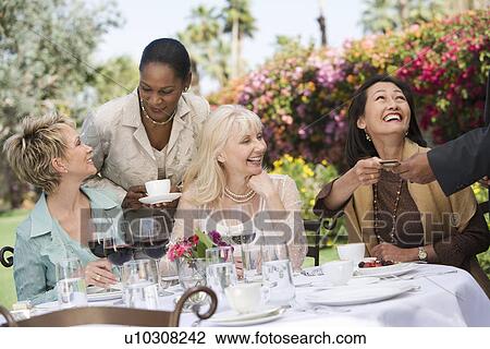 Stock Image - Female friends drinking at outdoor table. Fotosearch