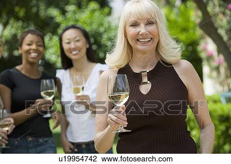 Stock Image - Female friends holding wine outdoors, portrait. Fotosearch
