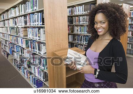 Picture - Female student choosing books in library. Fotosearch