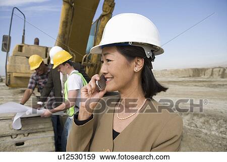 Stock Photo - Female surveyor and construction workers on site. Fotosearch