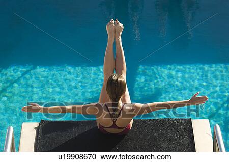Stock Image - Female swimmer sitting on diving board. Fotosearch