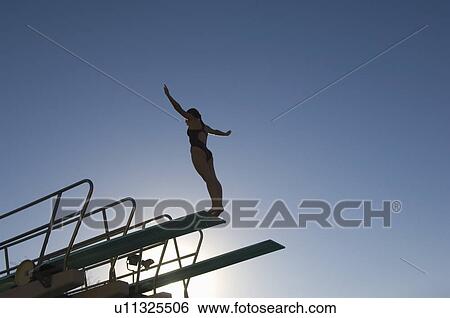 Stock Photograph - Female swimmer standing on diving board at sunset. Fotosearch