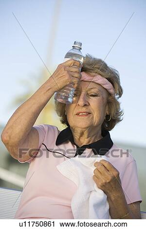 Stock Image - Female tennis player putting bottle of water to forehead. Fotosearch