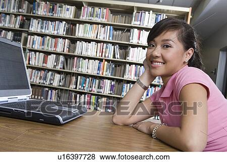 Stock Photo - Female university student with laptop in library. Fotosearch