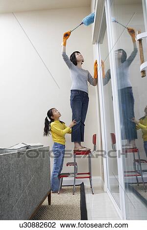 Stock Image - Girl (7-9) helping mother with dusting, side view. Fotosearch