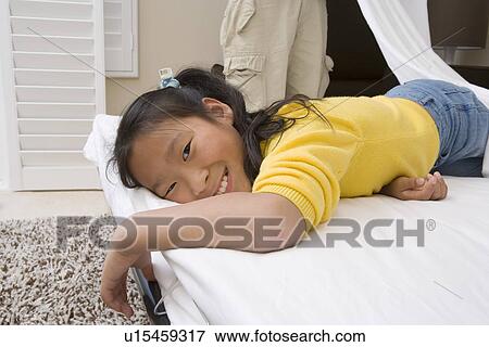 Stock Photo - Girl lying down on bed and smiling. Fotosearch
