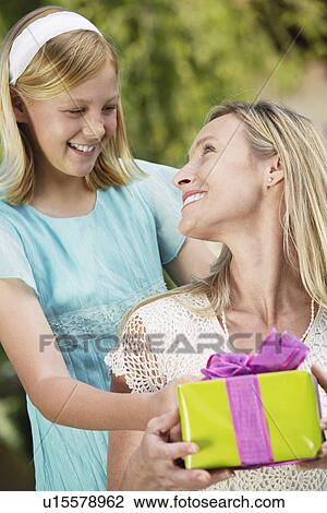 Girl standing behind mother, giving gift. Mother looking over shoulder, smiling View Large Photo Image Stock Image - Girl standing behind mother, giving gift. Mother looking over shoulder, smiling. Fotosearch