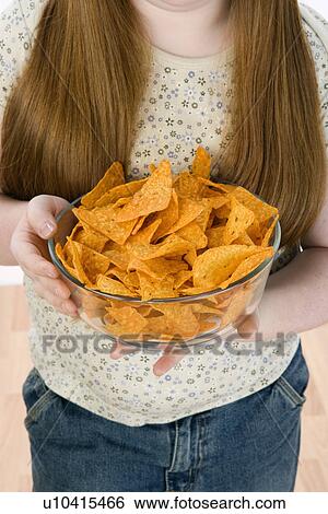 Stock Photograph - Girl standing, holding bowl of potato chips, mid section. Fotosearch