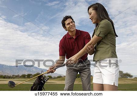 Stock Photography - Golf coach assisting mid-adult woman with swing. Fotosearch