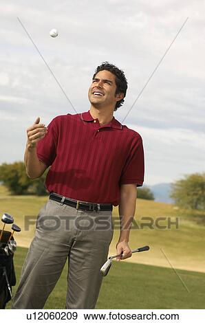 Stock Photo - Golfer Holding Putter Tossing Golf Ball in Air on golf course. Fotosearch