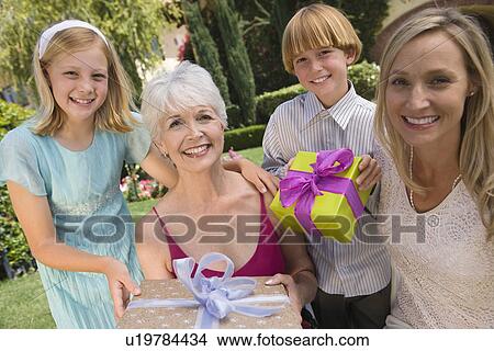Grandmother with daughter and grandchildren in garden holding birthday present View Large Photo Image Picture - Grandmother with daughter and grandchildren in garden holding birthday present. Fotosearch