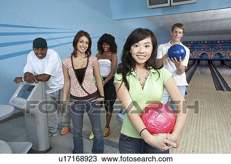 Stock Image - Group of friends at bowling alley, some holding balls, portrait. Fotosearch